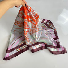 Load image into Gallery viewer, A satin head scarf with a geometric pattern in multiple colors, predominantly purple, orange, and green, being held up by a person.