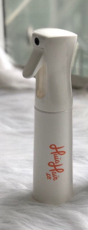 A white curly spray mist bottle designed for hair use, displaying the brand name 'Huia' on its side.