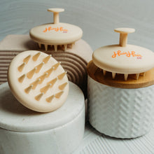 Load image into Gallery viewer, A silicone scalp massage brush with a beige handle and bristles, placed on a textured surface.
